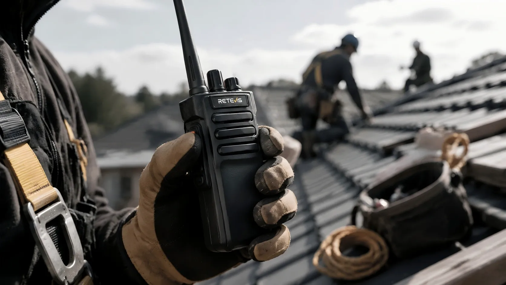Close-up of a roofer using a waterproof push-to-talk walkie-talkie with belt clip on a rooftop jobsite.
