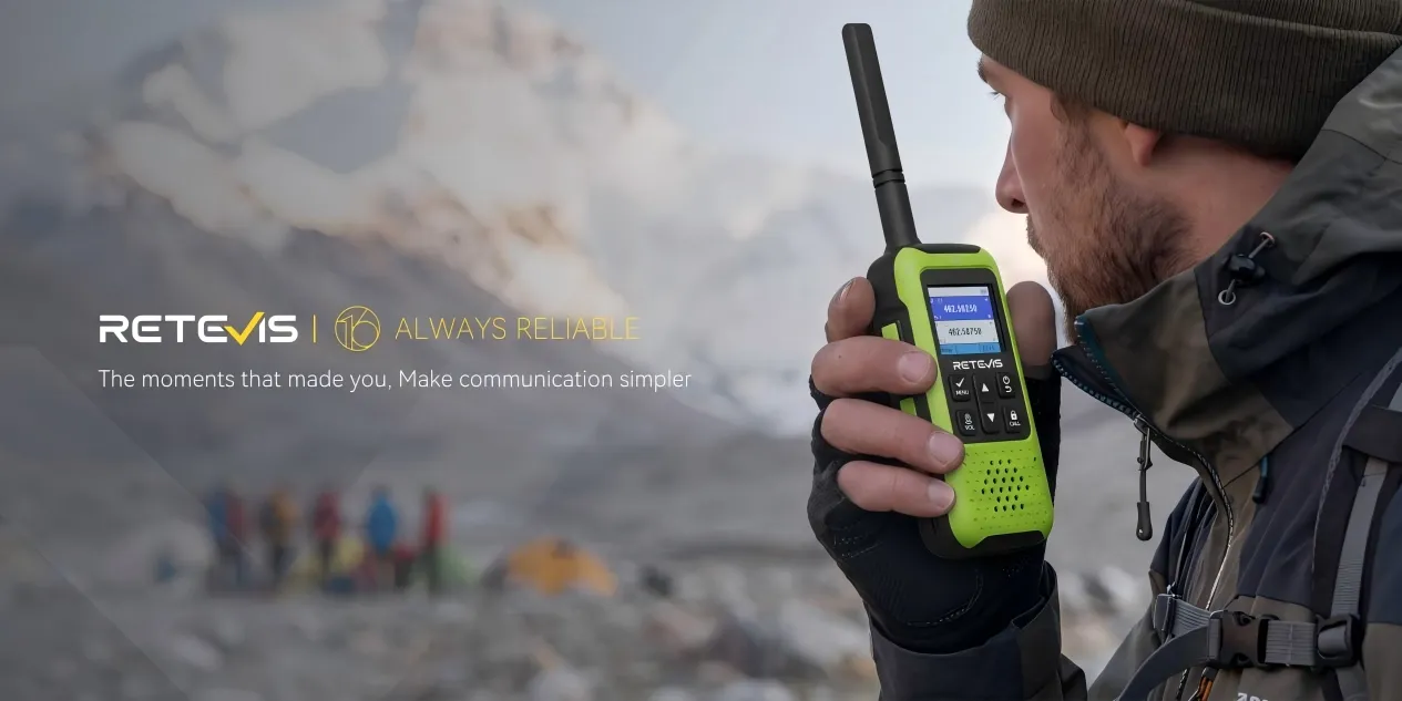 Hiker using a Retevis walkie talkie in the mountains with snowy peaks in the background.